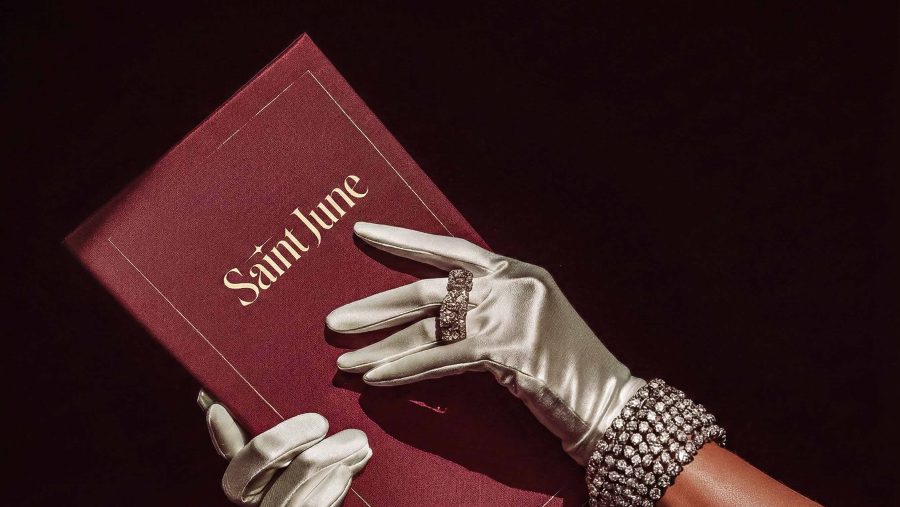The Saint June identity manual, a deep red book beside a gloved hand and jewellery